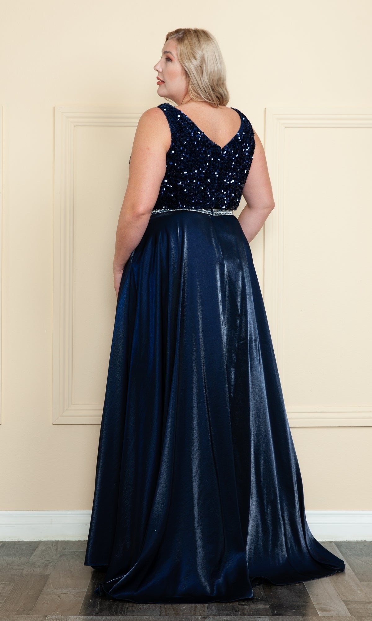 A woman faces away, wearing the Plus-Size Long Sequin-Bodice Prom Dress W1006 in navy blue, featuring a sequined bodice, rhinestone belt, and flowing satin skirt.